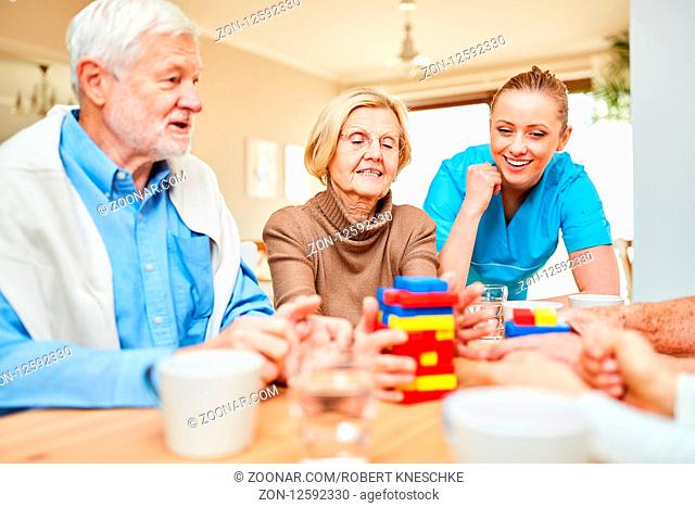 Dementes Senioren Paar und Pflegehilfe spielen mit bunten Bausteinen im Pflegeheim