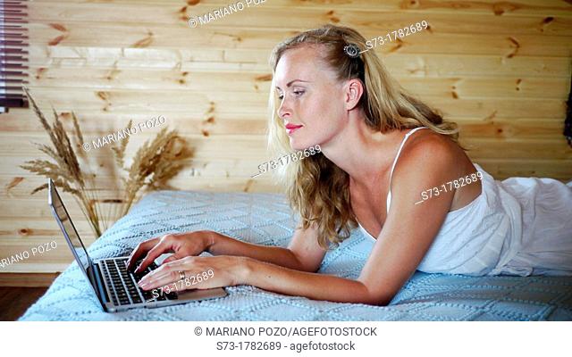 Young beautiful happy woman lying on the bed with laptop