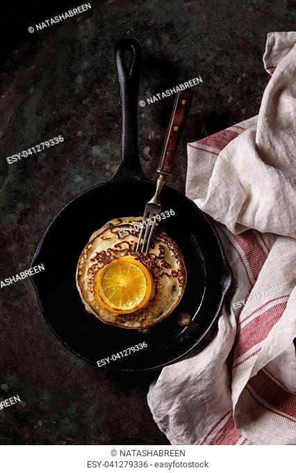 Homemade pancakes with fried orange, served in cast-iron pan on kitchen towel over dark old rusty background. Top view with space. Dark rustic style