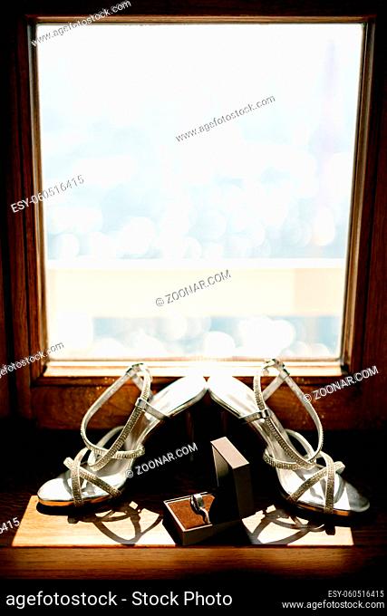 Bridal sandals on a wooden windowsill with wedding rings in a box. High quality photo