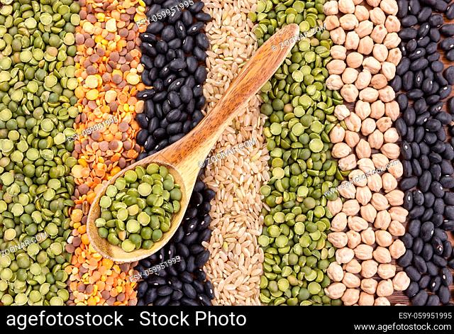 Neatly laid out rows of assorted dried grains and a wooden spoon with split peas in it