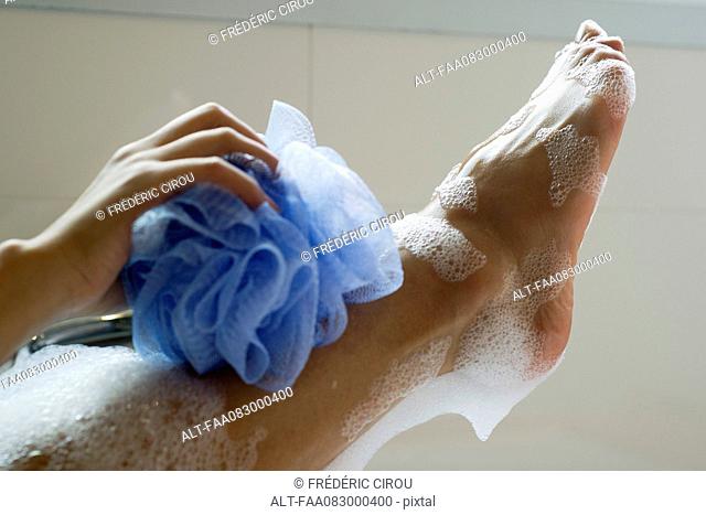 Woman washing foot with bath sponge, cropped