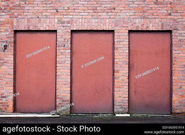 Three red metal doors in old brick wall