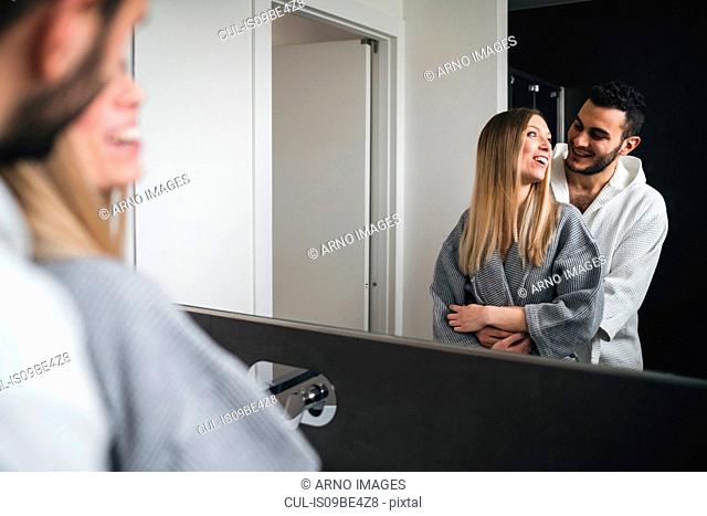 Mirror image of couple hugging in bathroom