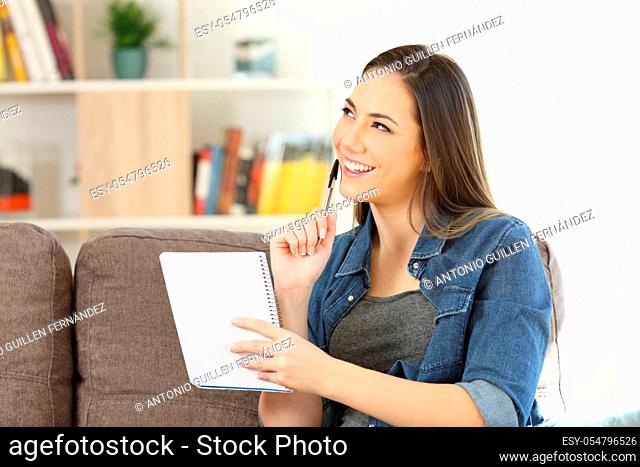 Pensive girl holding notebook looking at side sitting on a sofa in the living room at home
