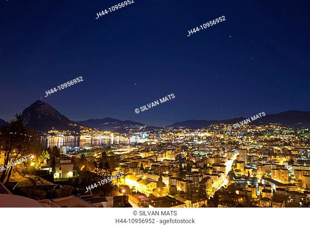 Cityscape at night close to a lake with mountain and with star trails over lugano ticino Switzerland, Europe