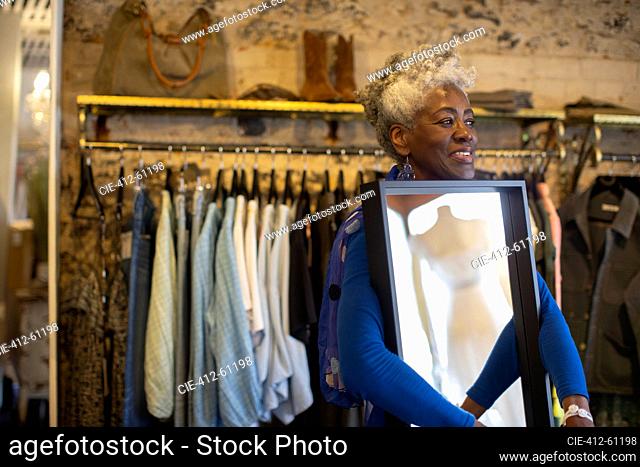Smiling senior female shop owner with mirror in boutique