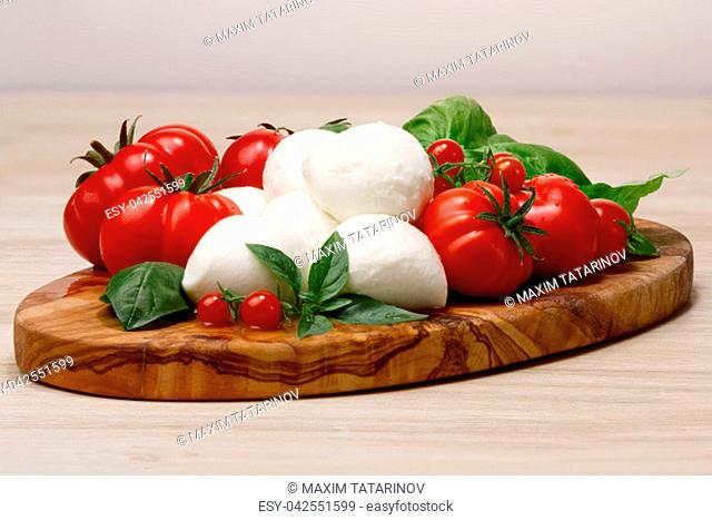 Italian cuisine. Mozzarella, heirloom tomatoes, basil leaves on a wooden serving plate. Large depth of field