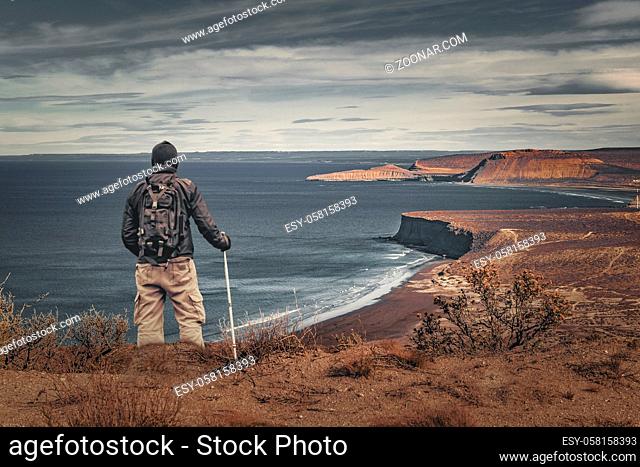 Man at top of mountain holding walking stick watching the seascape.Chubut, Patagonia