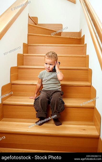 Little boy sitting on stairs, playing with portable phone