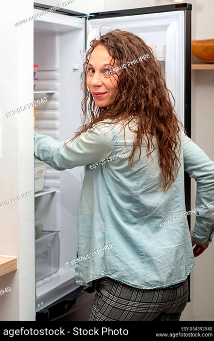 Modern attractive woman with long hair in the kitchen opening the frige door