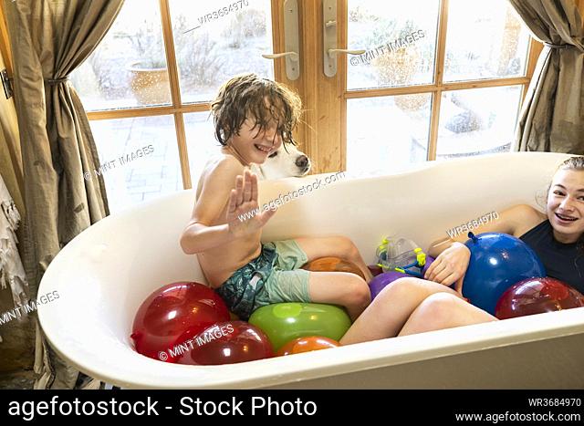 Young boy and his older sister in bathtub filled with water balloons