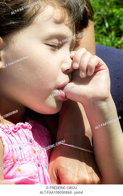 Little girl asleep on mother's lap, sucking thumb, cropped