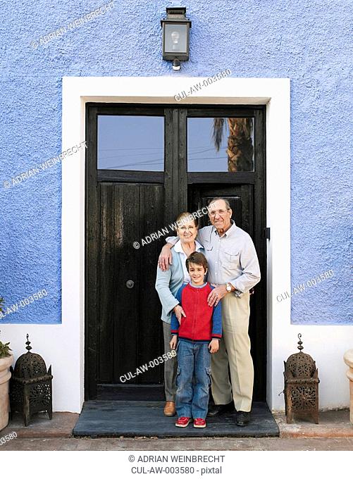 Grandparents and grandson 6-8 standing at front door, portrait