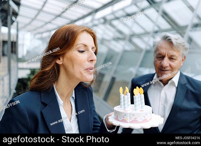 Businessman and businesswoman celebrating birthday in office with fake birthday cake