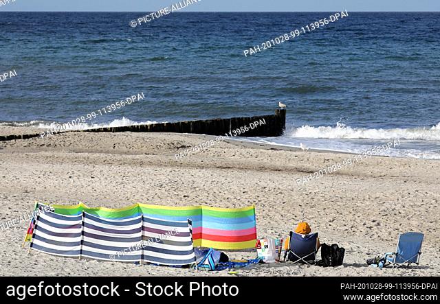 28 October 2020, Mecklenburg-Western Pomerania, Graal-Müritz: A beach visitor is sitting on a camping chair in the sand of the Baltic Sea