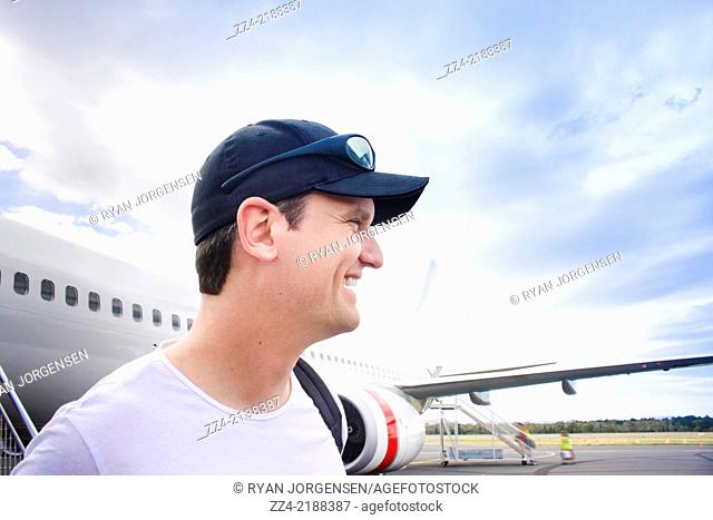 Candid travel lifestyle photo of a smiling man standing on airport tarmac having just stepped off airplane in an arrivals concept