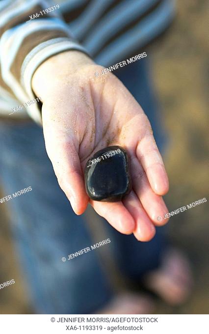 A young boy's sandy hand holds a shiny wet black stone