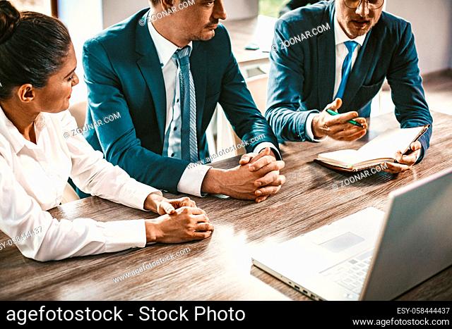 Business Group Brainstorming While Sitting At Office Desk, Colleagues Listen To Speaker, Intelligent Man Explaining Business Development Strategy While Looking...
