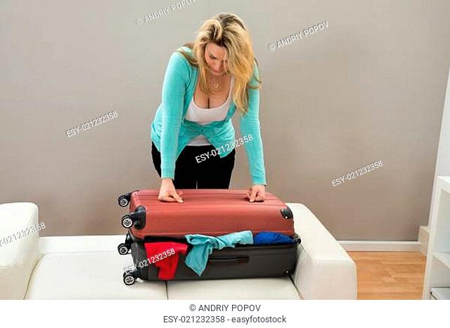 Woman Trying To Close The Overfilled Suitcase In The Room