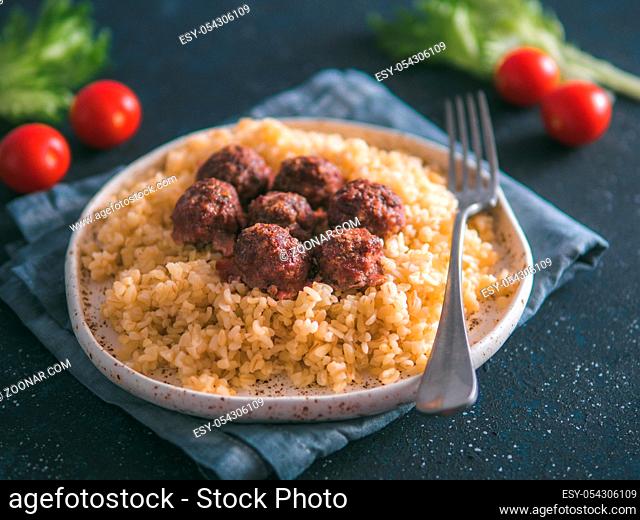 Bulgur dish idea and recipe. Bulgur with homemade roasted beef meatballs on dark blue background. Copy space for text. Shallow DOF