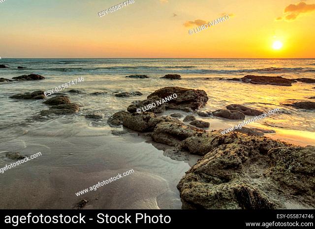 Beach in low tide, sand and rocks covered with algae showing from water, during golden sunset light. Koh Lanta, Thailand