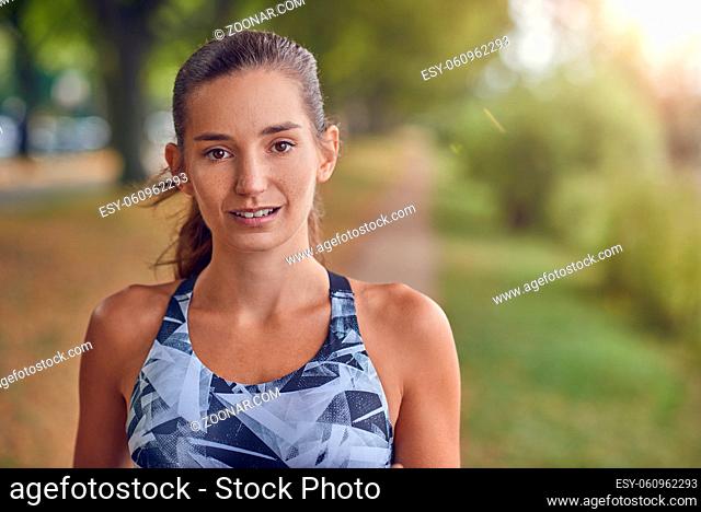 Attractive young woman iin sports attire and a ponytail standing outdoors in a rural park looking pensively at the camera in a close up head and shoulders...