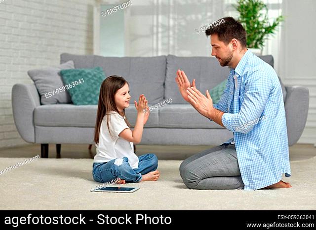Little kid girl plays with father at home sitting on white carpet. Father's day