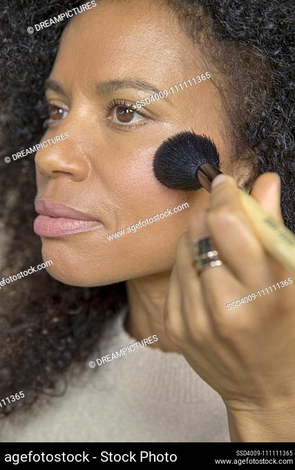 Mixed race, middle-aged woman looks off camera while putting on make up