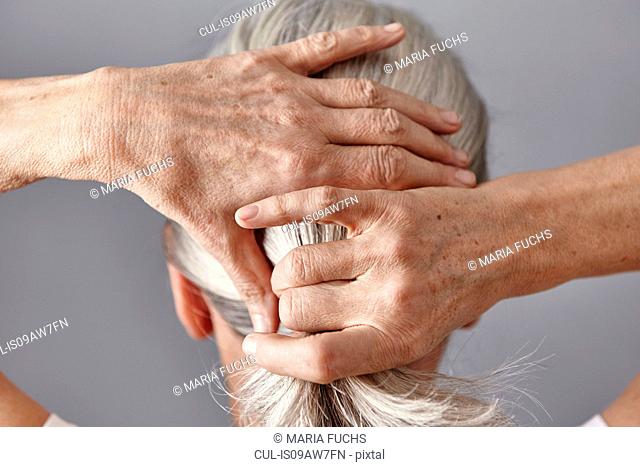 Rear view of woman pulling back gray hair into ponytail