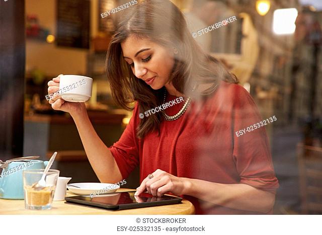 Woman Viewed Through Window Of Café Using Digital Tablet