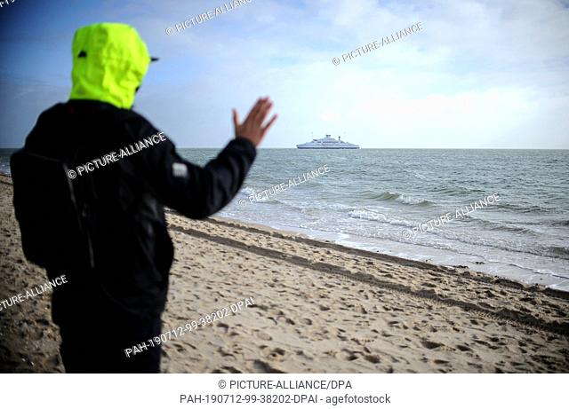 19 February 2019, Schleswig-Holstein, Sylt: A young man looks over the sea and waves to a ferry. Sylt is the largest North Frisian island in Germany