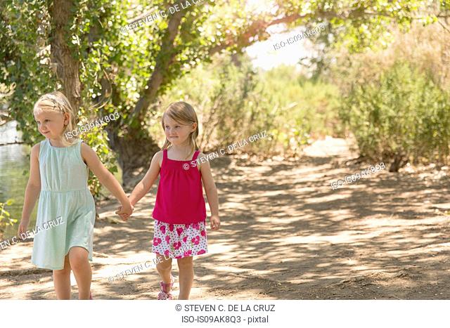 Two young sisters strolling and holding hands on riverbank