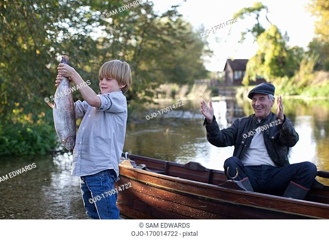 Grandson catching fish with grandfather cheering in background
