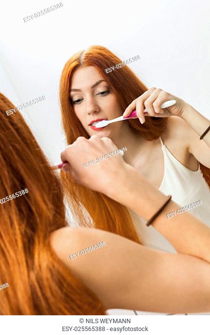 attractive young woman in the morning when brushing your teeth in the mirror in bathroomwith long red hair