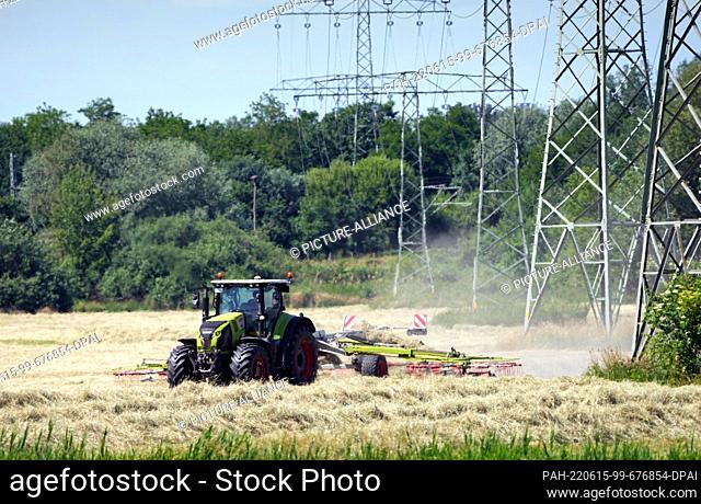 14 June 2022, Brandenburg, Potsdam: A farmer drives across a field with a trailed rotary windrower on the edge of the Drewitz district next to electricity...