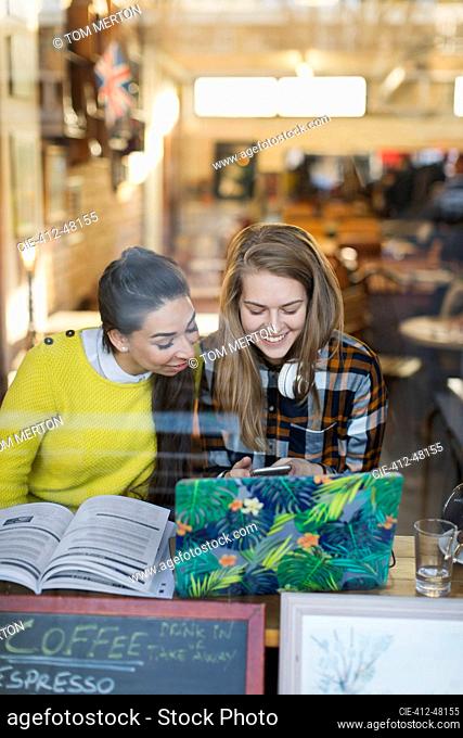 Smiling young female college students studying in cafe