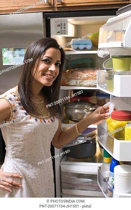 Portrait of a young woman standing and smiling in front of a refrigerator