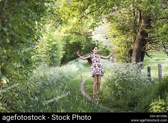 Young girl making a jump on a small country trail bordered by umbellifers on the edge of the forest, Eure-et-Loir department, Centre-Val-de-Loire region, France