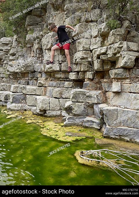 Boy climbing on a wall in a mountain river. Villahermosa river, Ludiente, Castellón, Spain