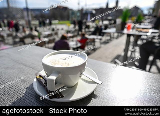 PRODUCTION - 16 March 2023, Baden-Württemberg, Landesweit: A cup of cappuccino stands on a table in an outdoor restaurant in Stuttgart
