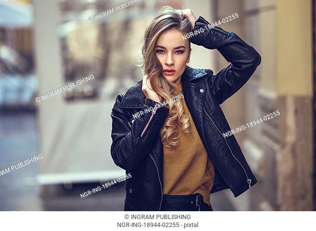 Blonde woman in urban background. Beautiful young girl wearing black leather jacket and mini skirt standing in the street
