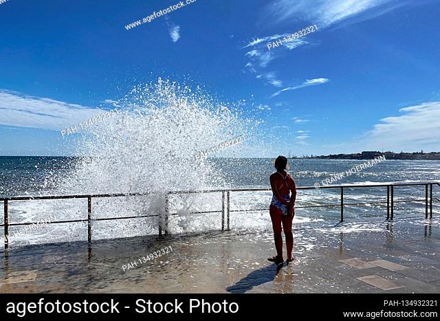 Little going on on Tamariz Beach in Estoril on 08/21/2020. Only a few tourists and locals go along the promenade - waves break over the parapet and water shoots...