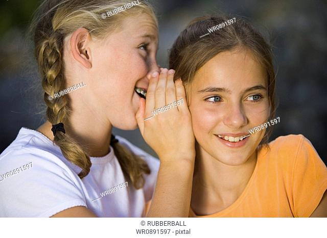 Close-up of a girl whispering into her friends ear