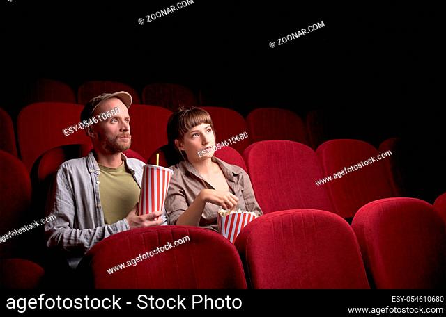 Young cute couple sitting alone at red movie theatre and having fun