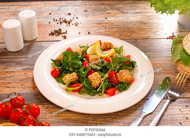 fresh salad of cherry tomatoes, croutons and capelin roe, mixed lettuce leaves in a white dish on an old wooden table, top view