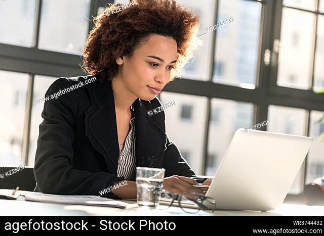 Portrait of African American female expert analyzing printed business report while sitting at desk in the office