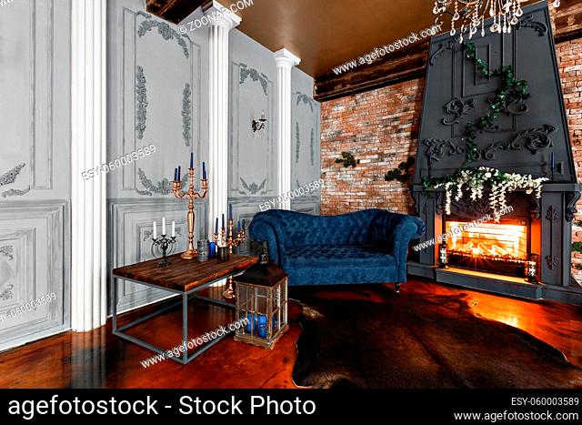 Interior with fireplace, candles, skin of cows, brick wall, large window and a metal cell of a loft, living room, coffee table and dark blue sofa in modern...
