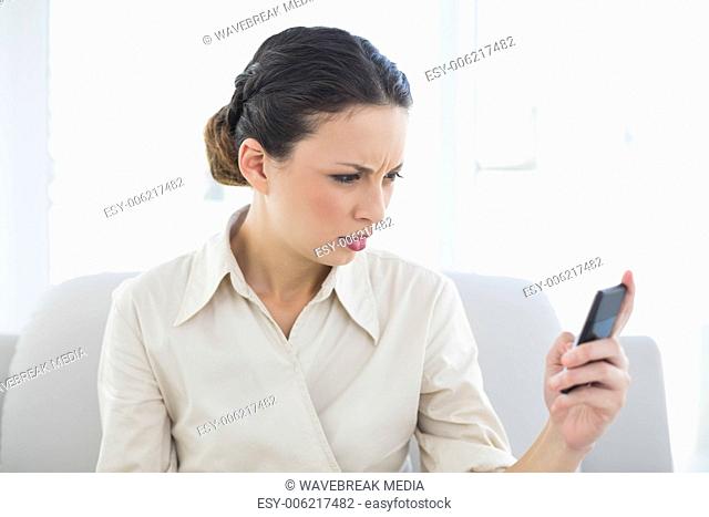 Frowning stylish brunette businesswoman looking at her mobile phone