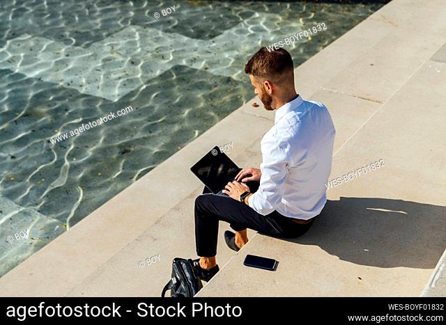 Mid adult businessman working on digital tablet while sitting on steps